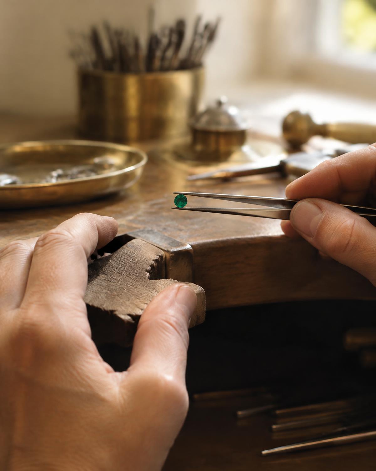 A jeweller holding a loose emerald at the bench